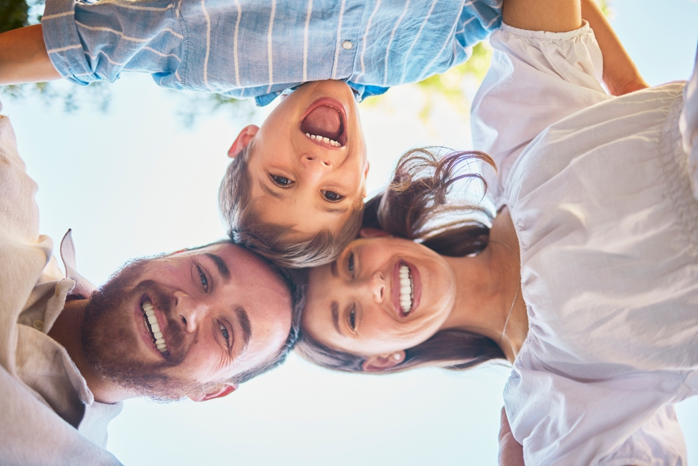 A joyful family of three in a huddle, smiling as they look down at the camera