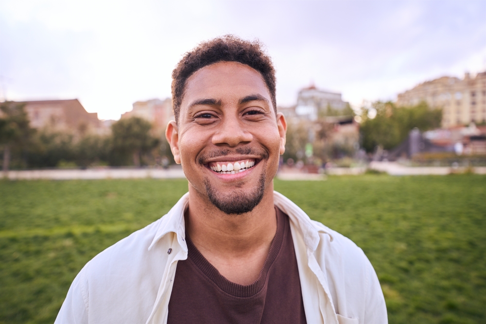 A confident young man with a brilliant, healthy smile outdoors, showcasing the beautiful results of Cosmetic Dentistry at Wilder Dentistry