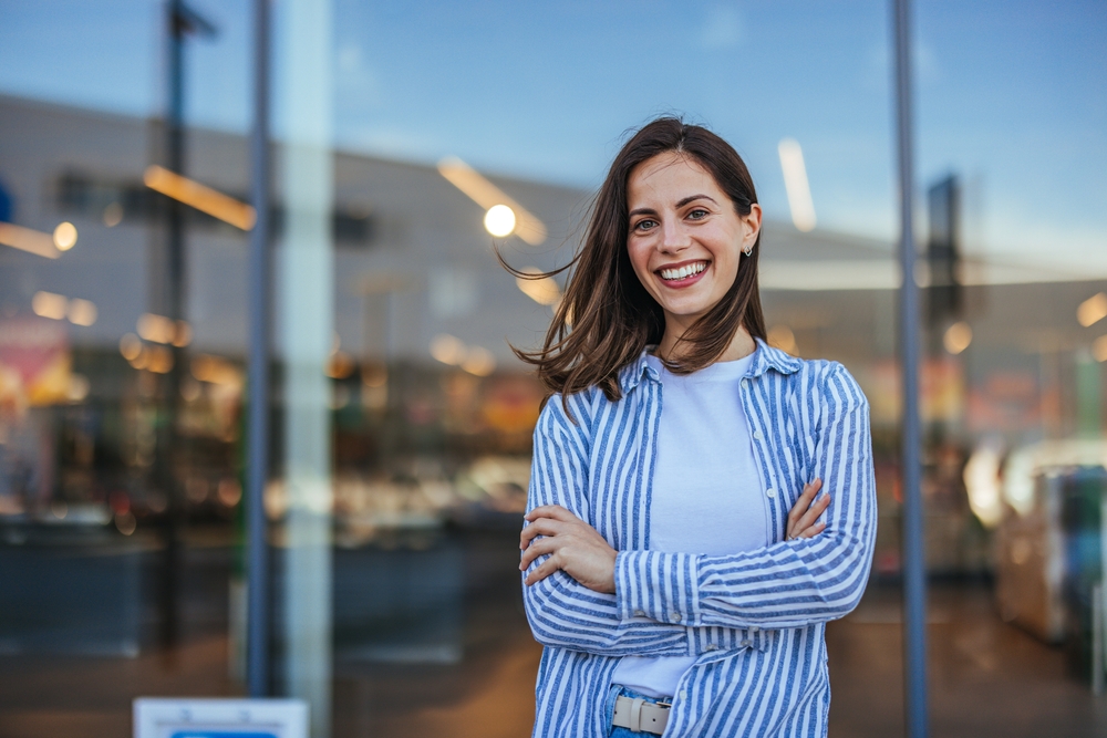 A confident woman with a flawless, beautiful smile stands in front of a modern building. Achieve your dream smile with custom-designed Veneers at Wilder Dentistry